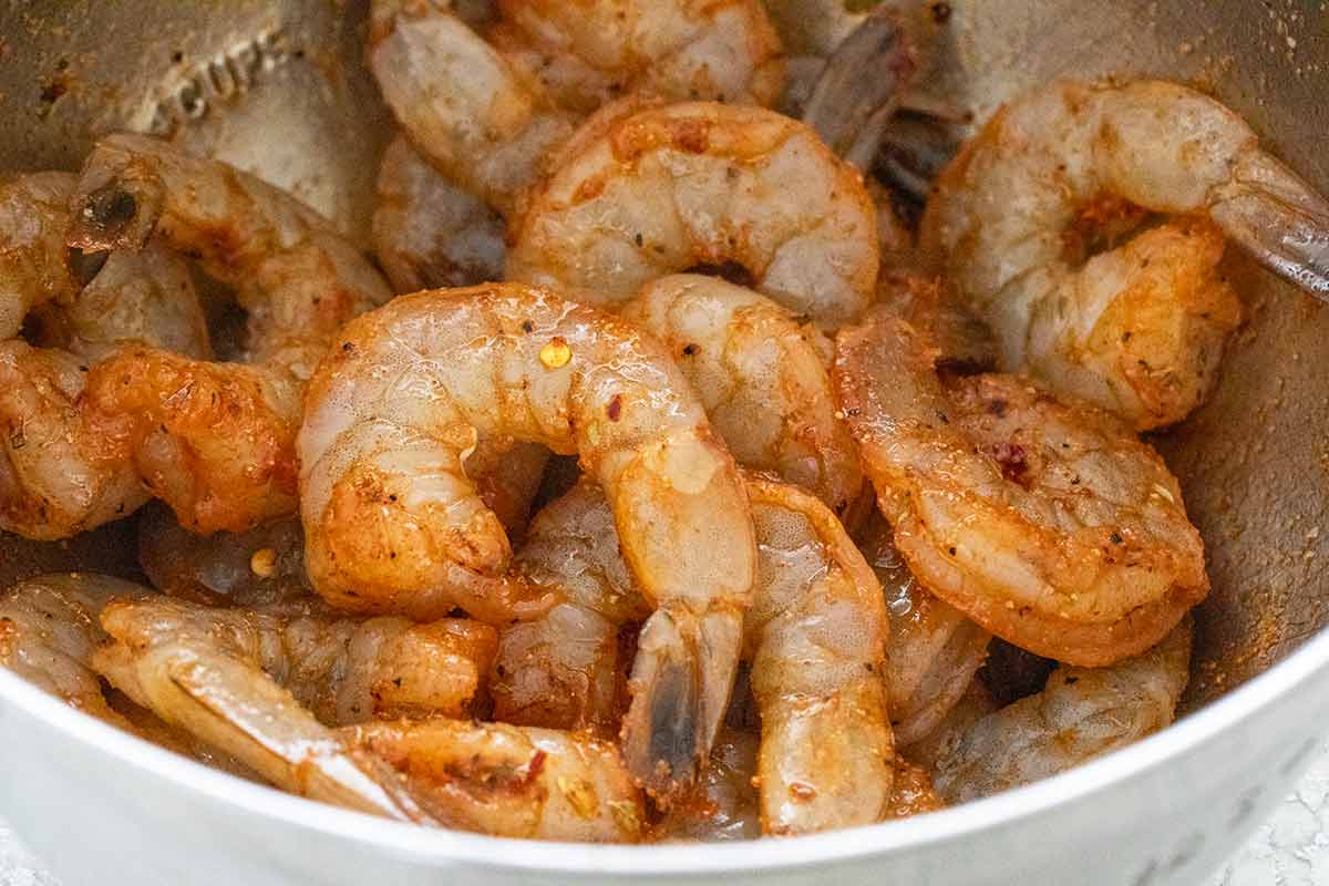 Raw shrimp marinating in a bowl of cajun seasonings.