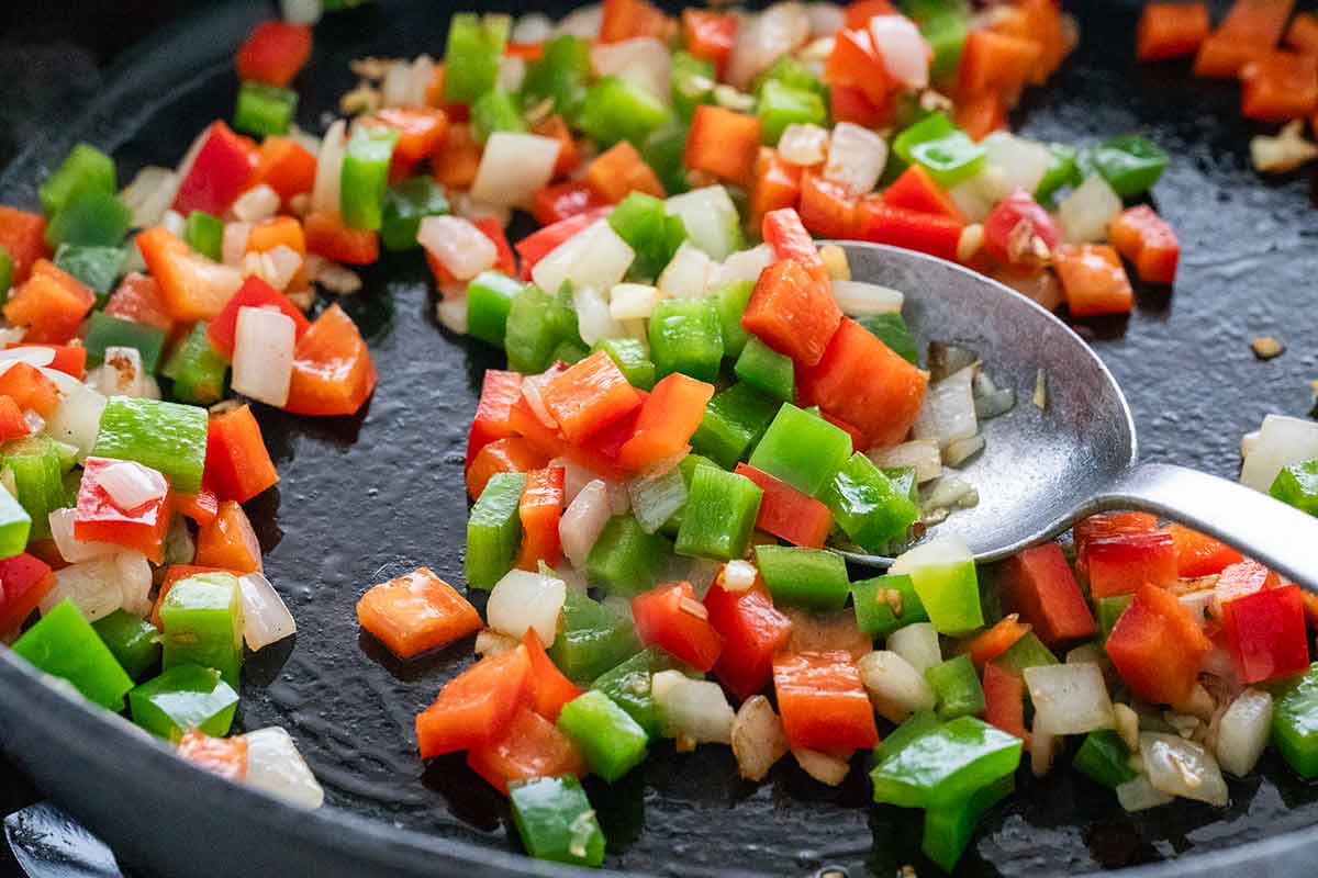 Cubes of bell peppers and onions sauteing in a cast iron skillet.