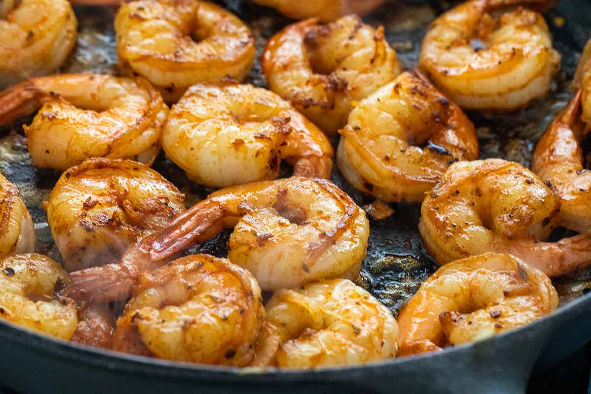 Several pieces of shrimp sauteing in a cast iron skillet.