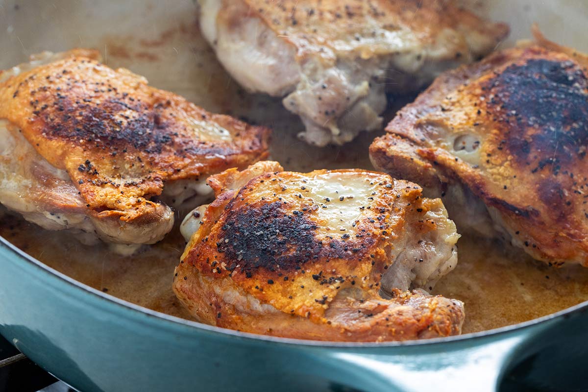 Searing bone-in chicken thighs skin-side down in a skillet until golden brown and crispy.