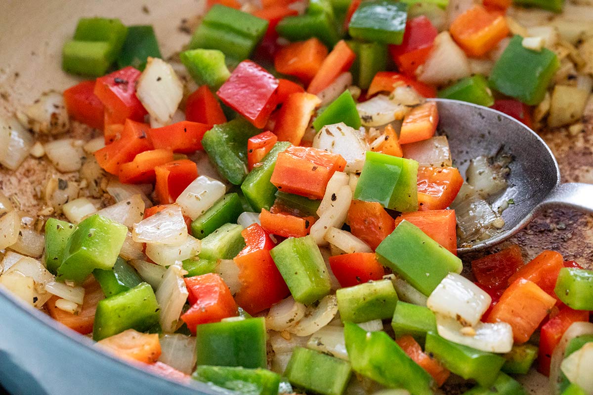 Diced red and green bell peppers and onions sautéing in a pan with herbs.