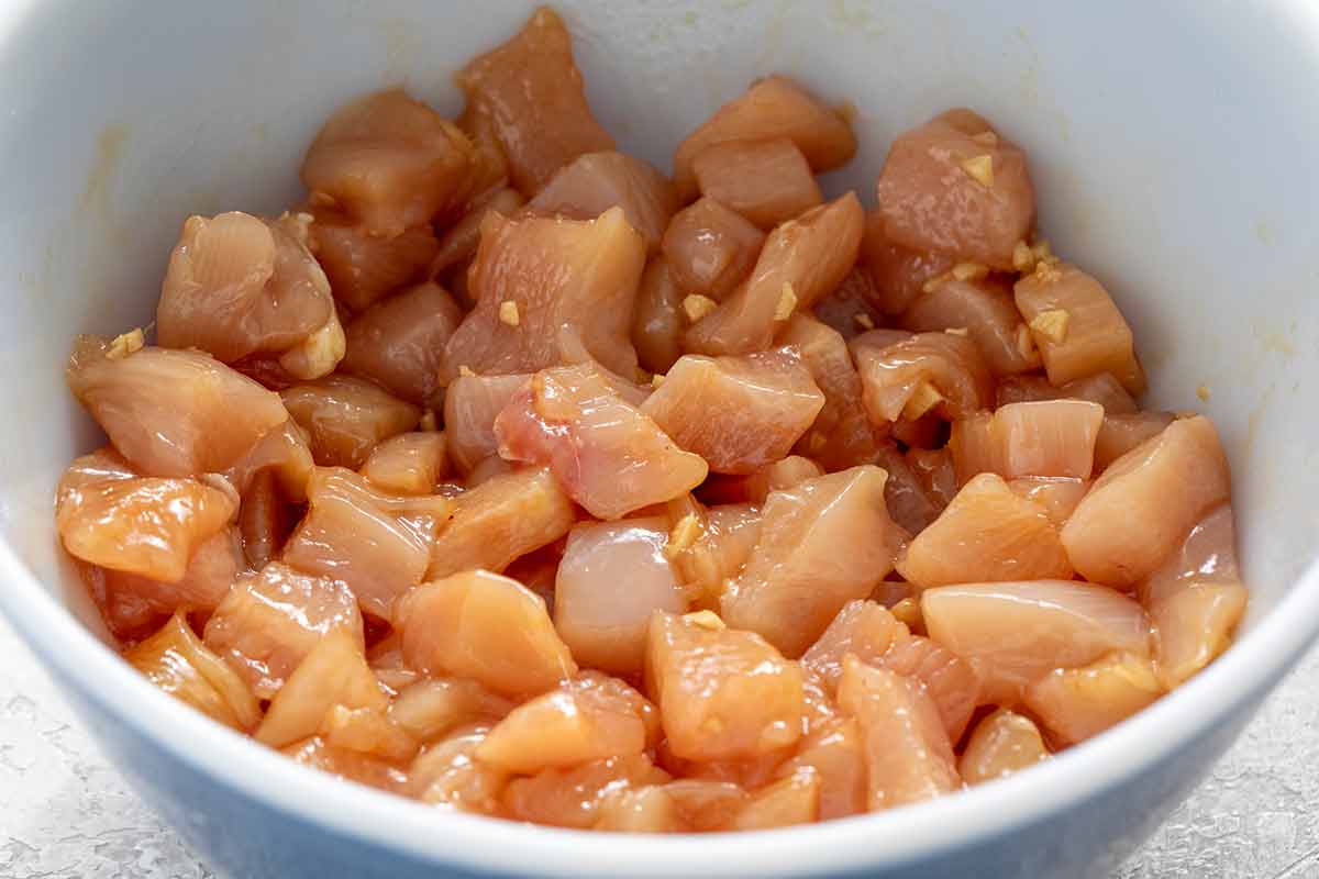 Chunks of boneless, skinless chicken breast marinating in a bowl.