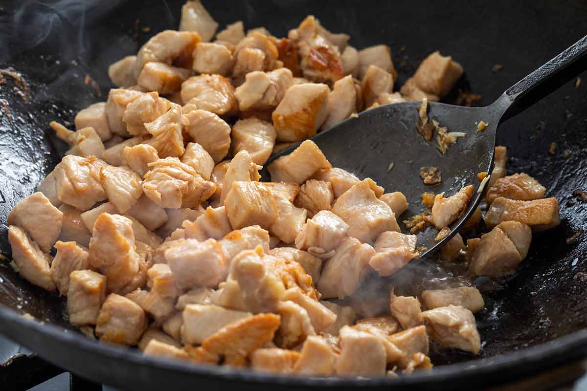 Cubes of chicken stir frying in a wok.
