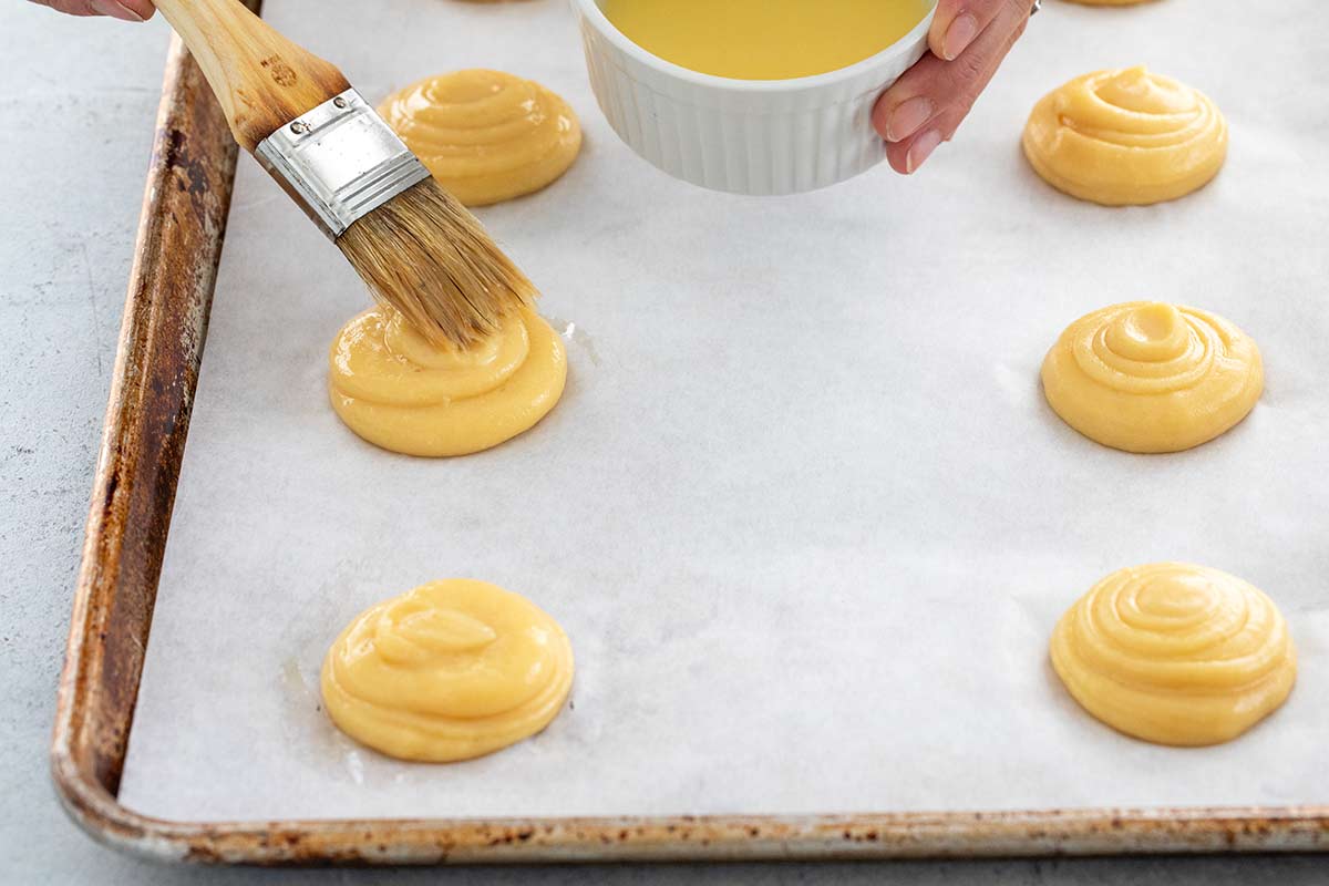 A brush applying egg wash to each puff pastry dough.