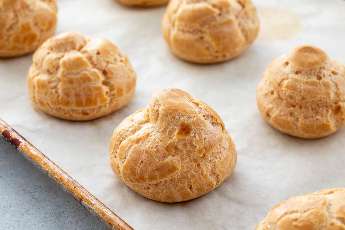Freshly baked cream puff shells lined up on a sheet pan.