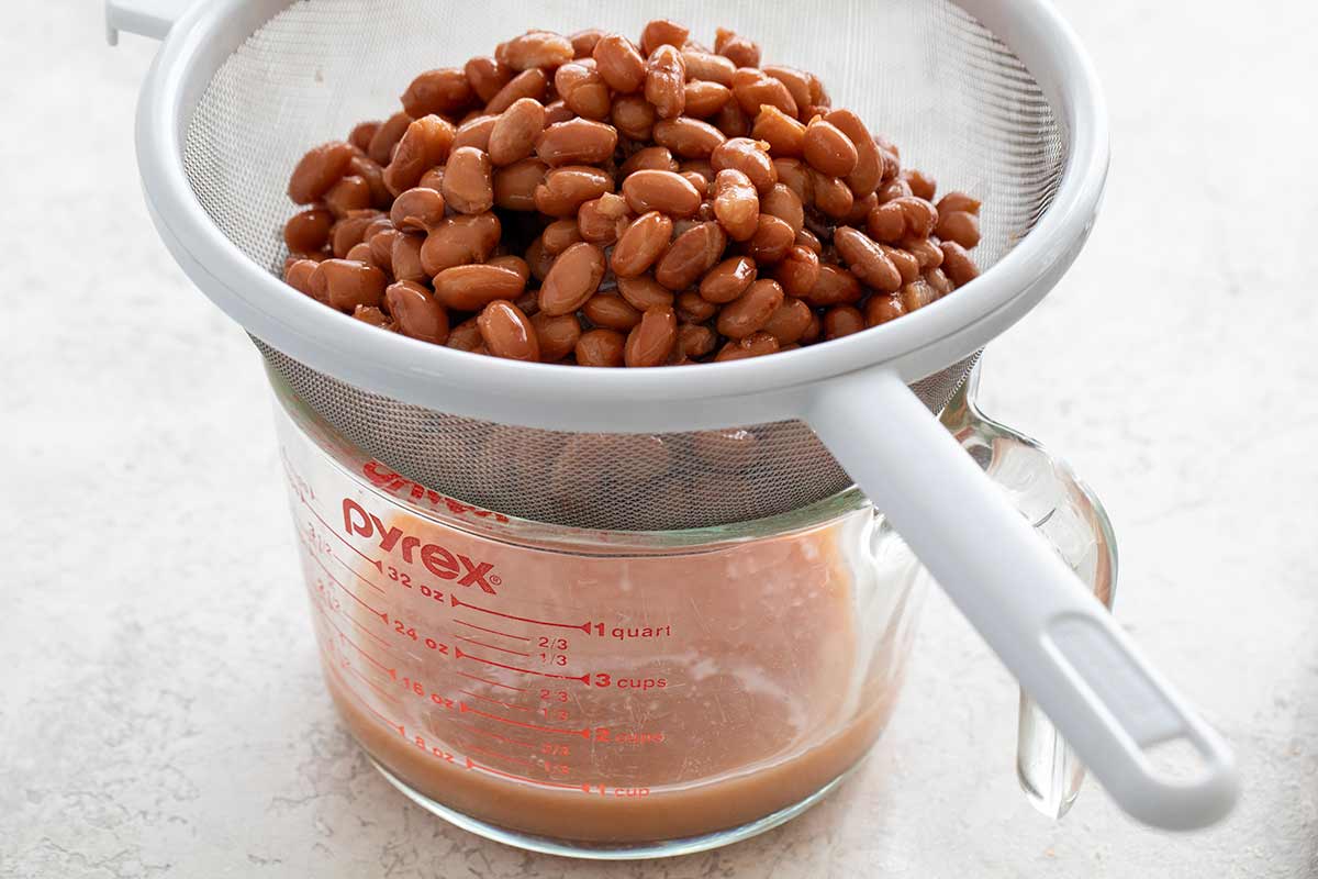 Beans inside a colander draining starchy liquid into a bowl.