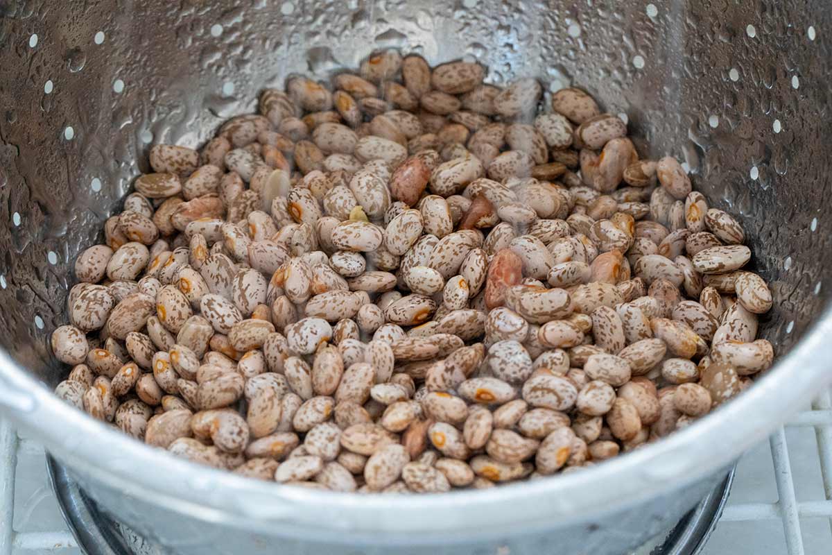 Beans in a metal colander being rinsed with water.