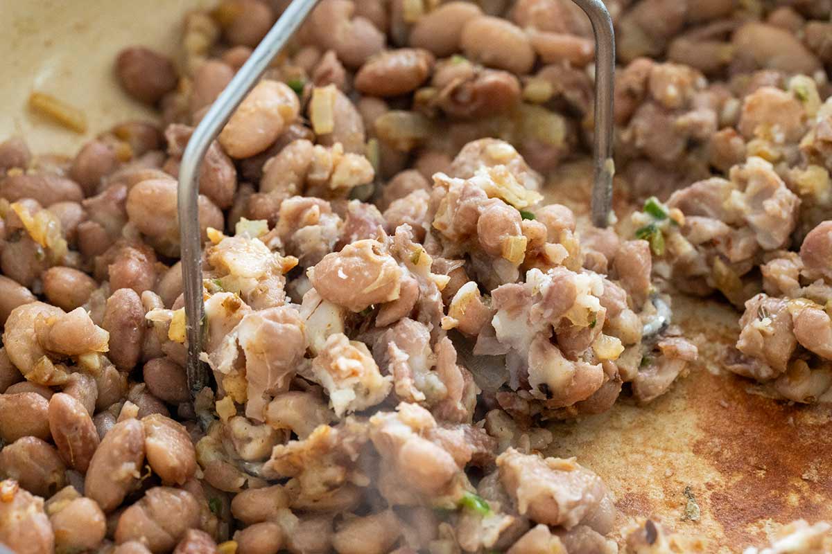 Potato masher pressing cooked beans in a pot.