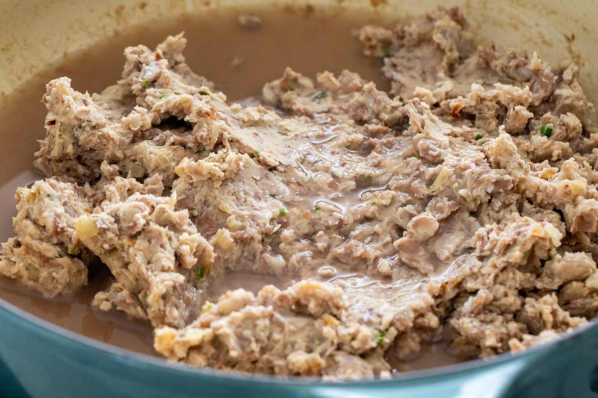 Starchy bean water added to a pot of mashed beans.