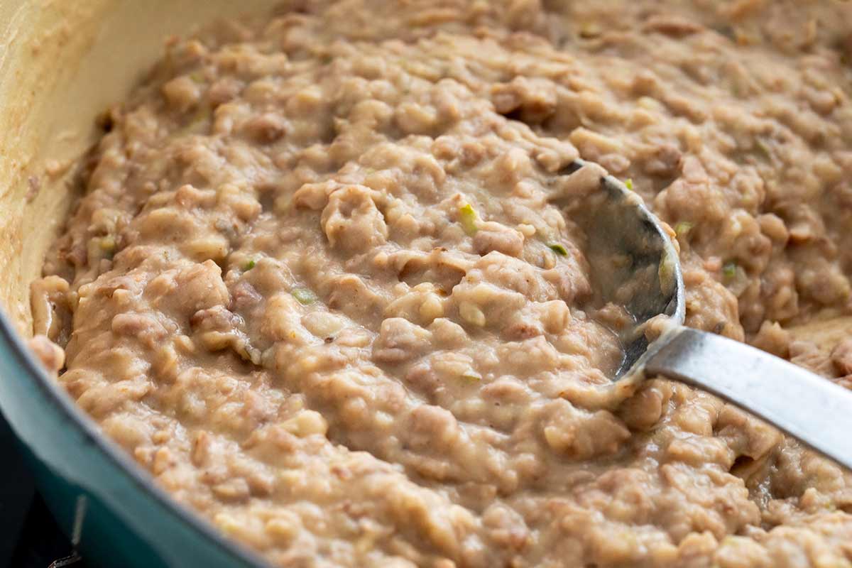 Metal spoon stirring a pot of homemade refried beans.
