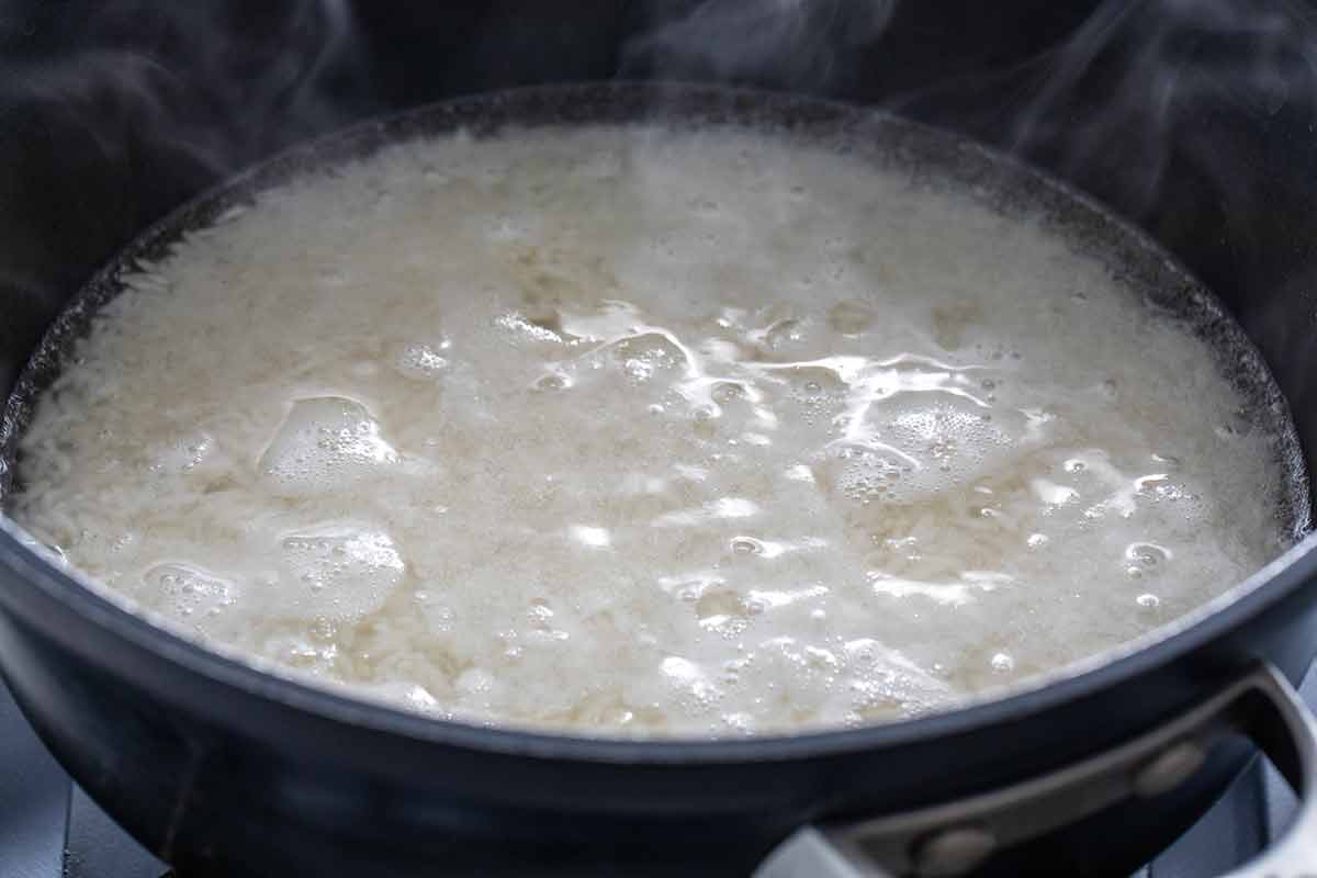 White rice simmering in a pot of bubbling water with steam rising