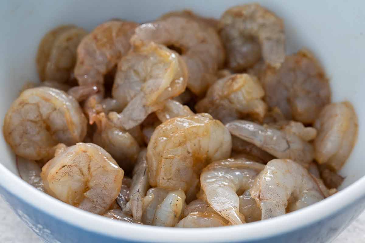 Raw peeled shrimp coated in seasoning marinade in a bowl