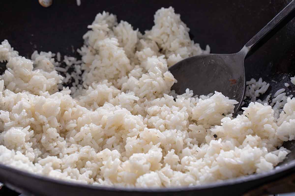 Stir-frying white rice with a spoon in a dark wok