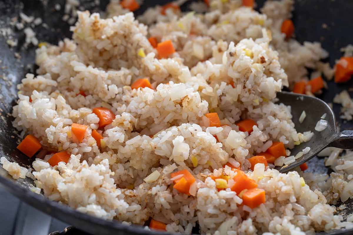 Rice and diced carrots being stir-fried in a wok with a spatula