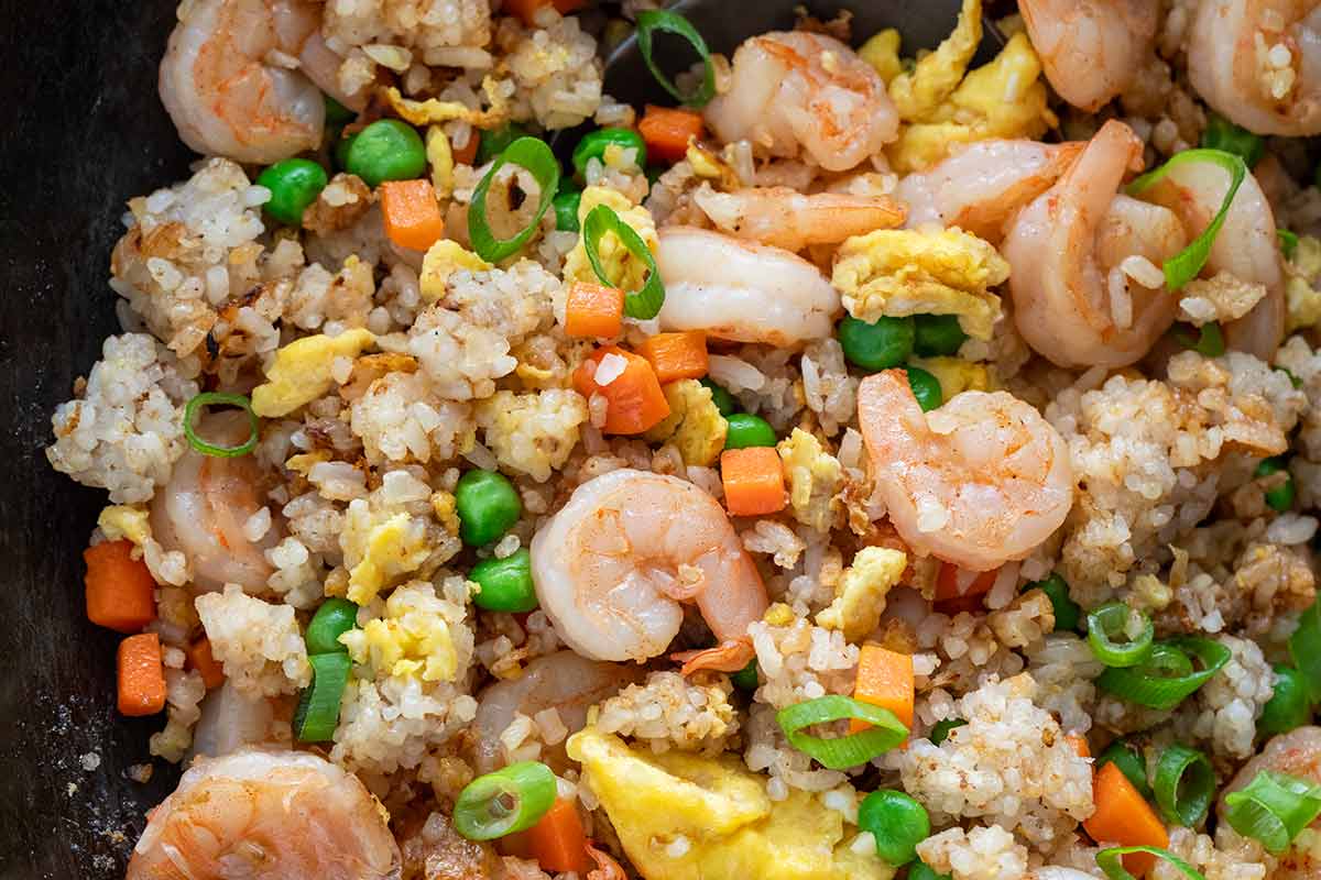 Close-up of cooked shrimp fried rice in a wok with scrambled eggs, green peas, carrots, and sliced green onions