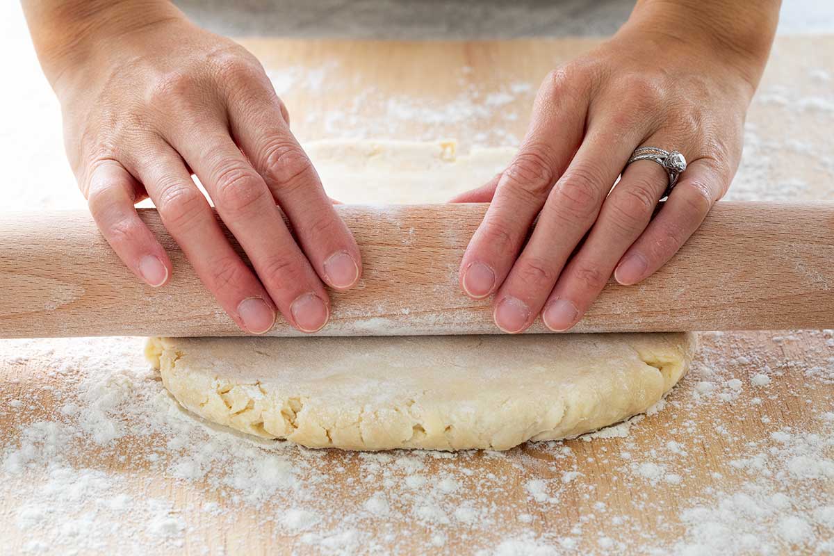 Pie dough being rolled using a floured rolling pin on a floured surface.