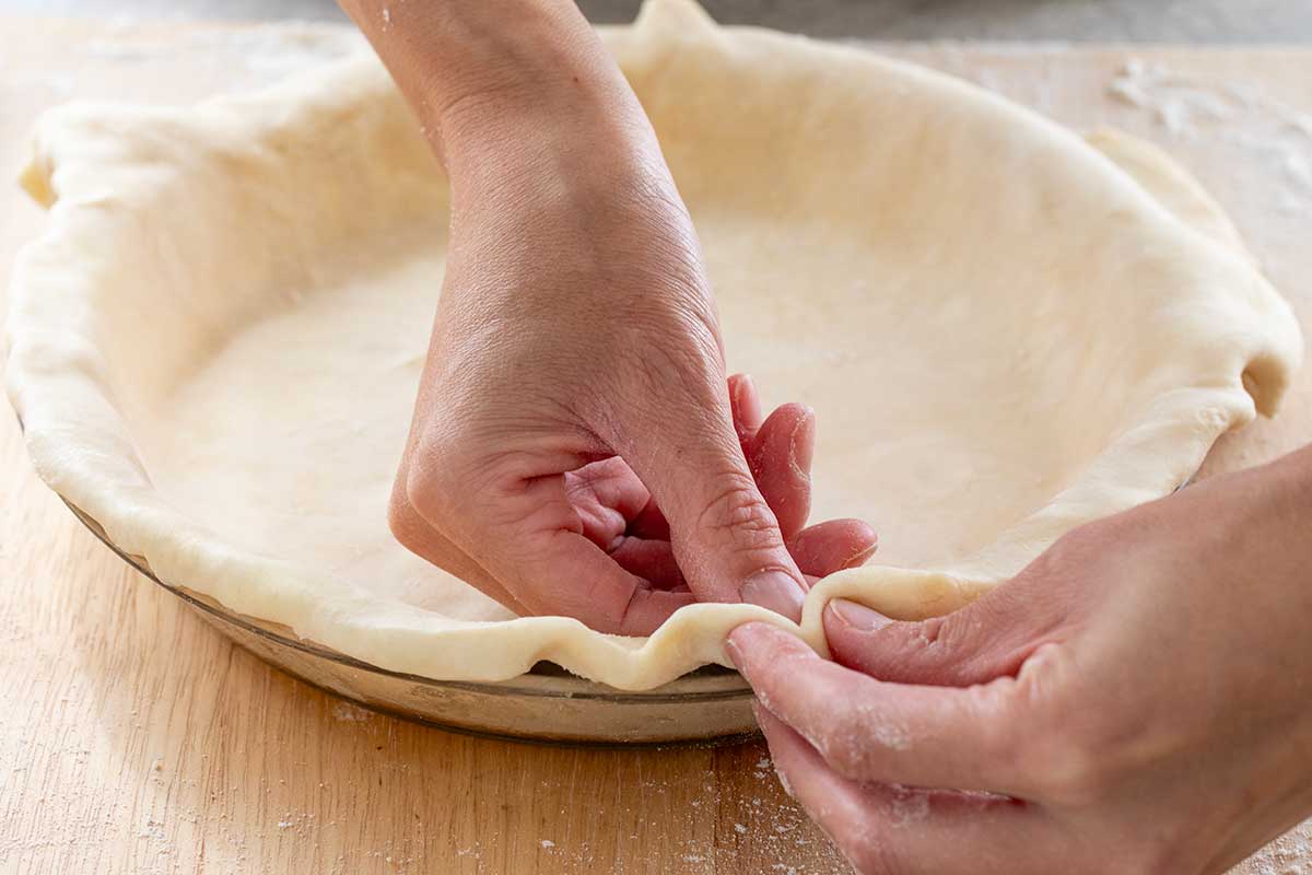 Fingers creating a fluted pattern around the edges of the pie crust.