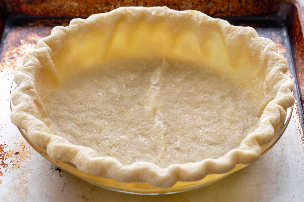 A par-baked pie crust with a fluted edge, ready to be filled with a ham and cheese quiche filling.