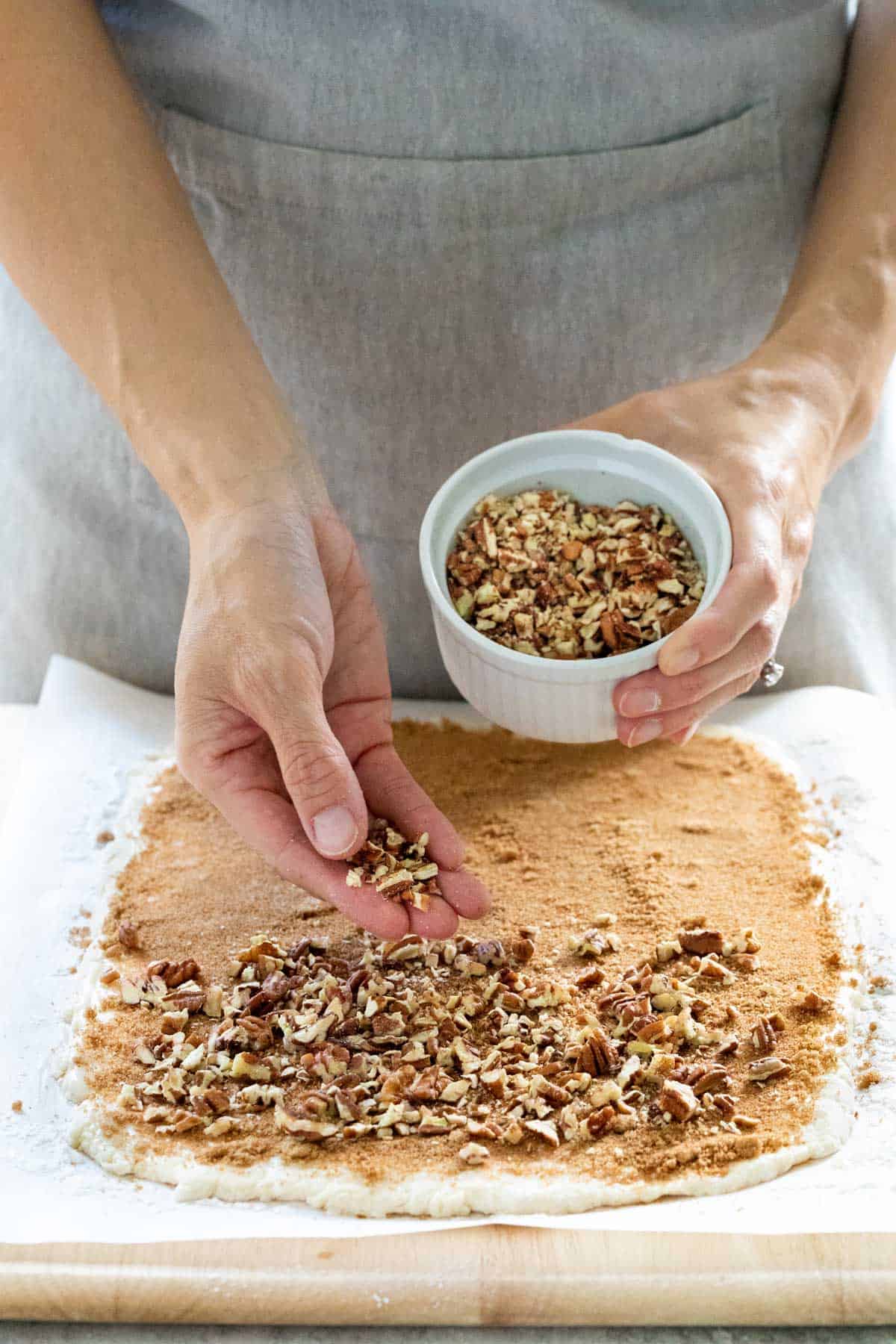 Person adding a layer of crushed pecans to the top of a piece of flattened dough.