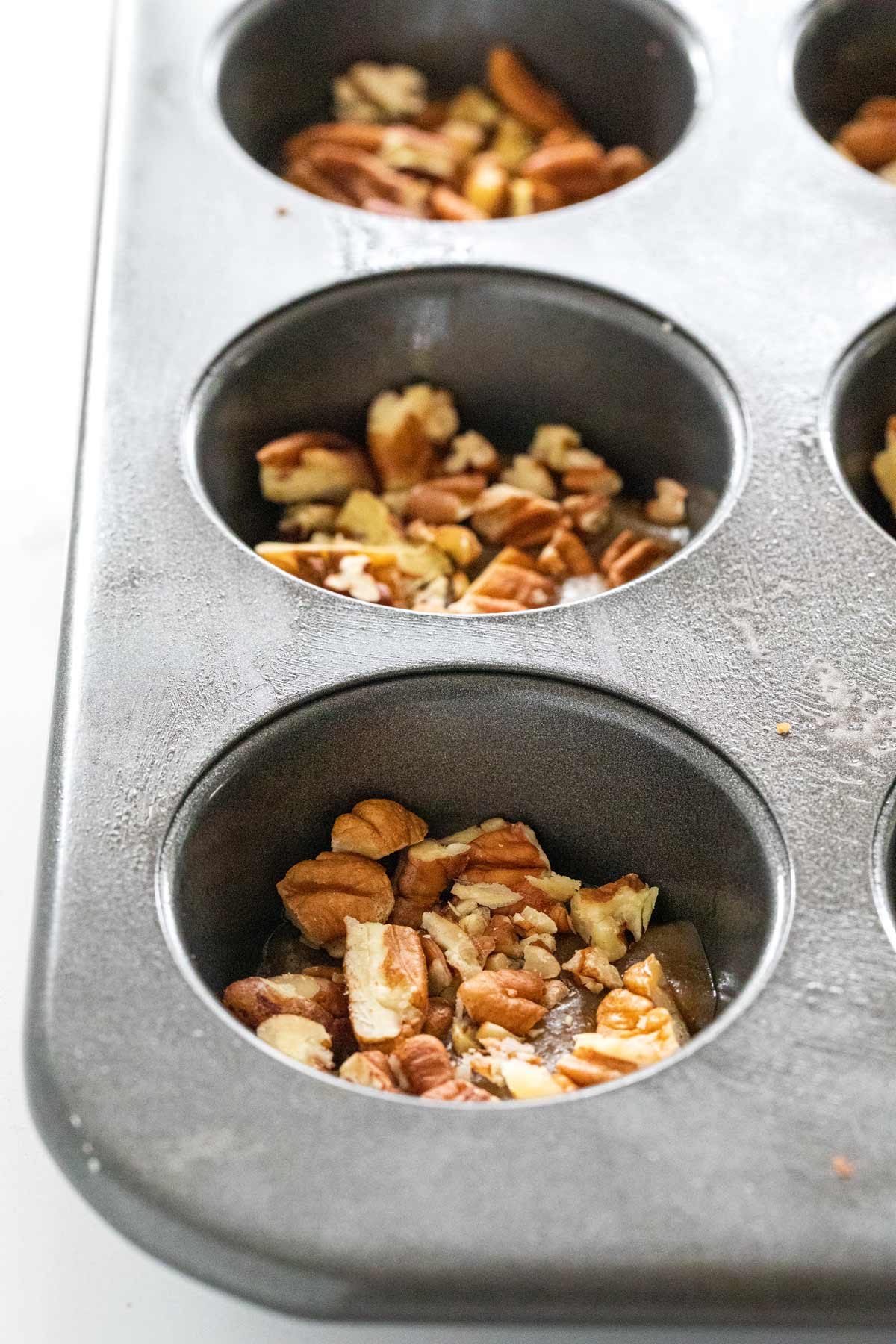 Muffin tin with caramel sauce and chopped pecans.