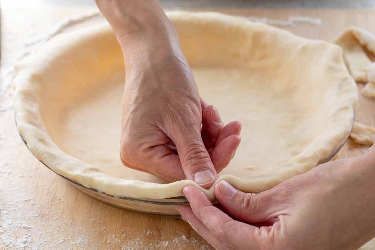 Jessica using her fingers to tuck the excess pie crust into the plate.