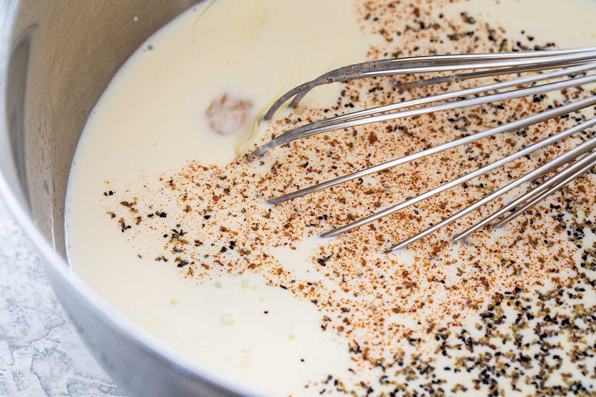 Whisking salt, pepper, and nutmeg into a mixture of eggs and heavy cream.