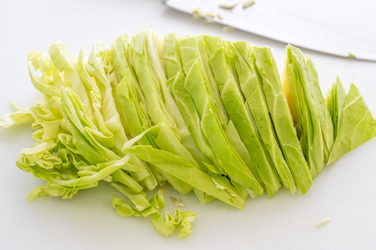 Fresh green cabbage sliced into thick strips on a cutting board.