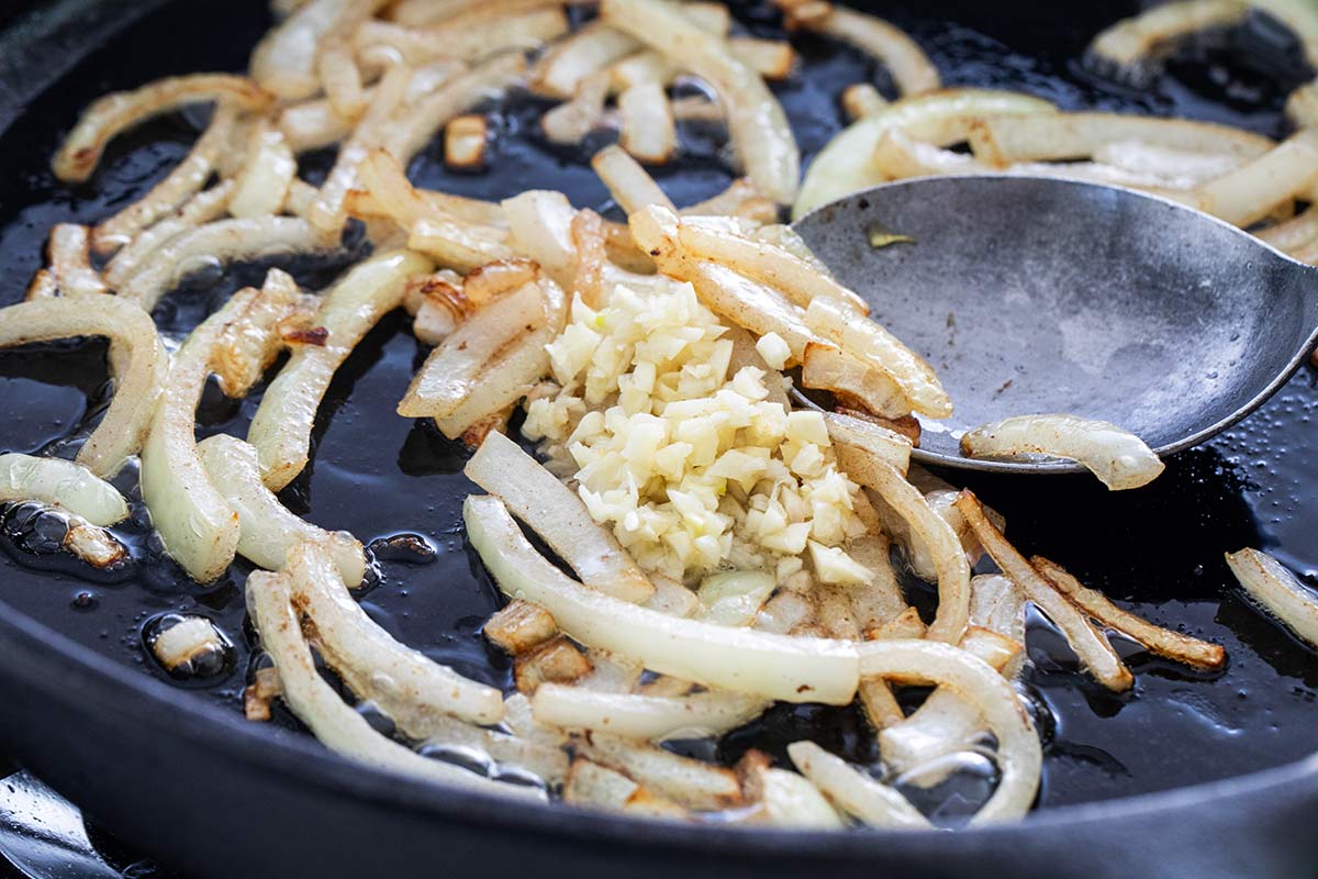 Sliced onions browning in a skillet with minced garlic added to the center.