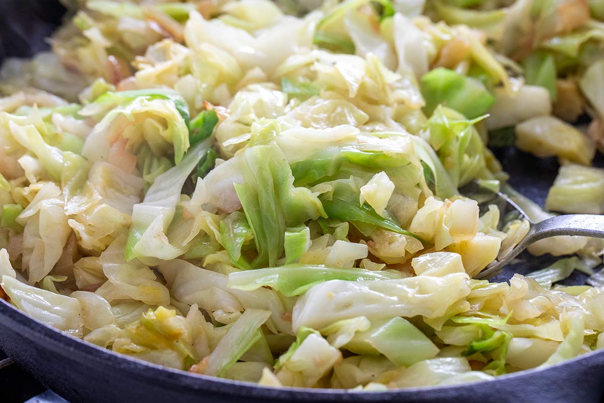 Shredded green cabbage and onions sautéing in a skillet.