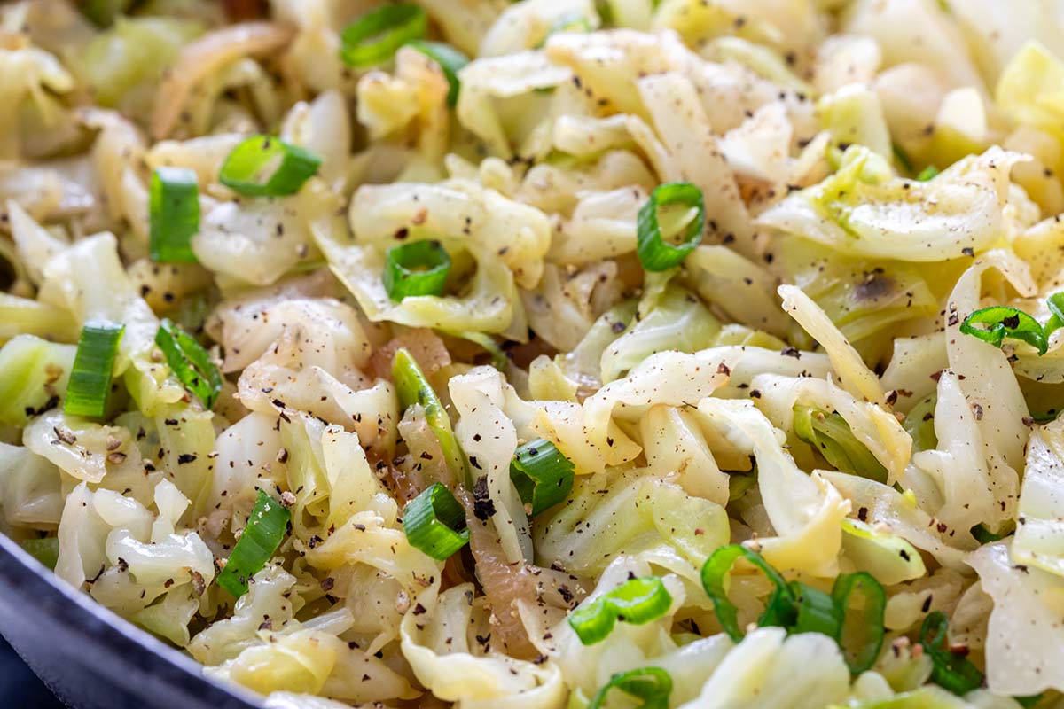 Close-up of tender sautéed green cabbage seasoned with cracked black pepper and garnished with sliced green onions.
