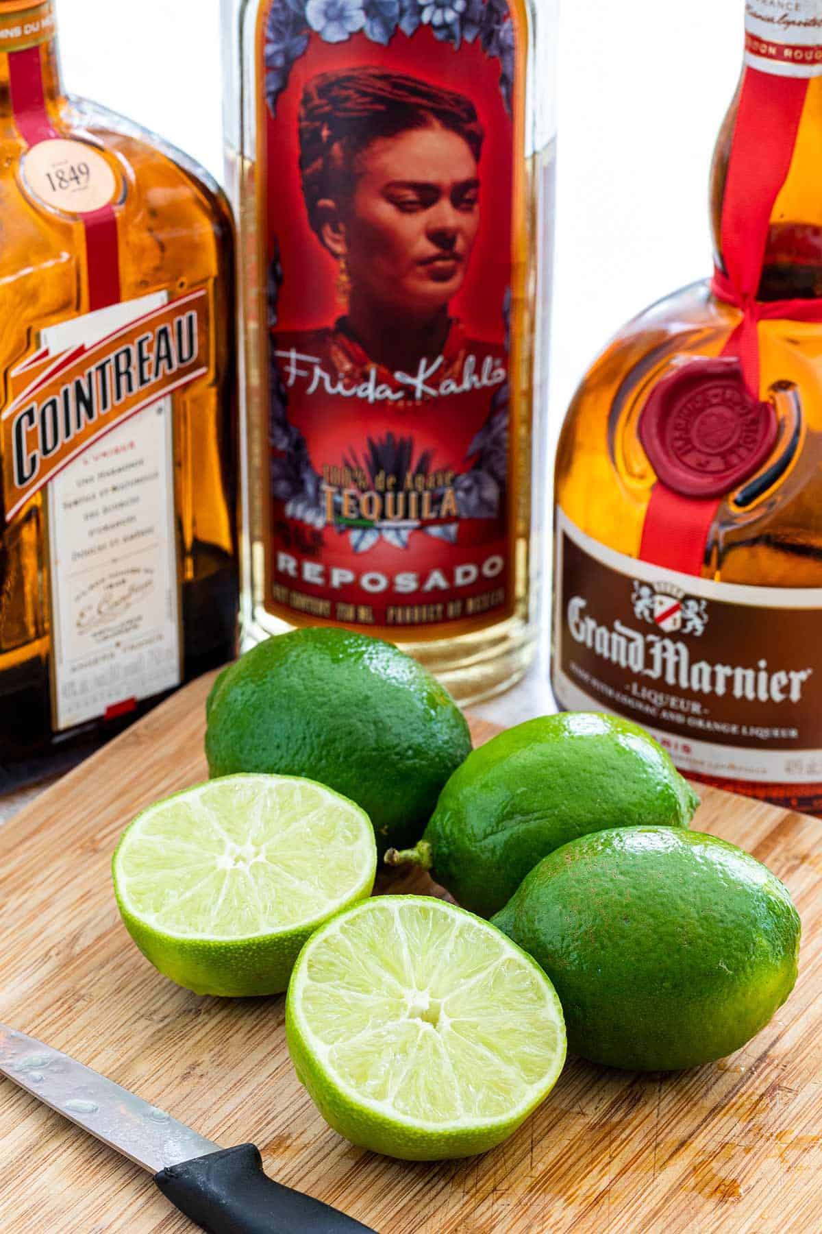 Sliced limes on a cutting board with alcohol bottles around it.
