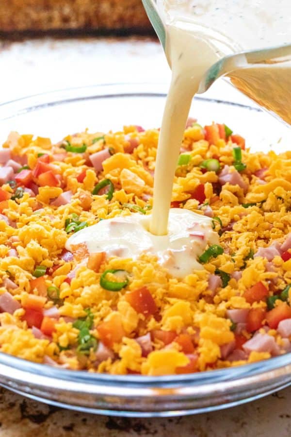 pouring egg mixture over cheese and ham