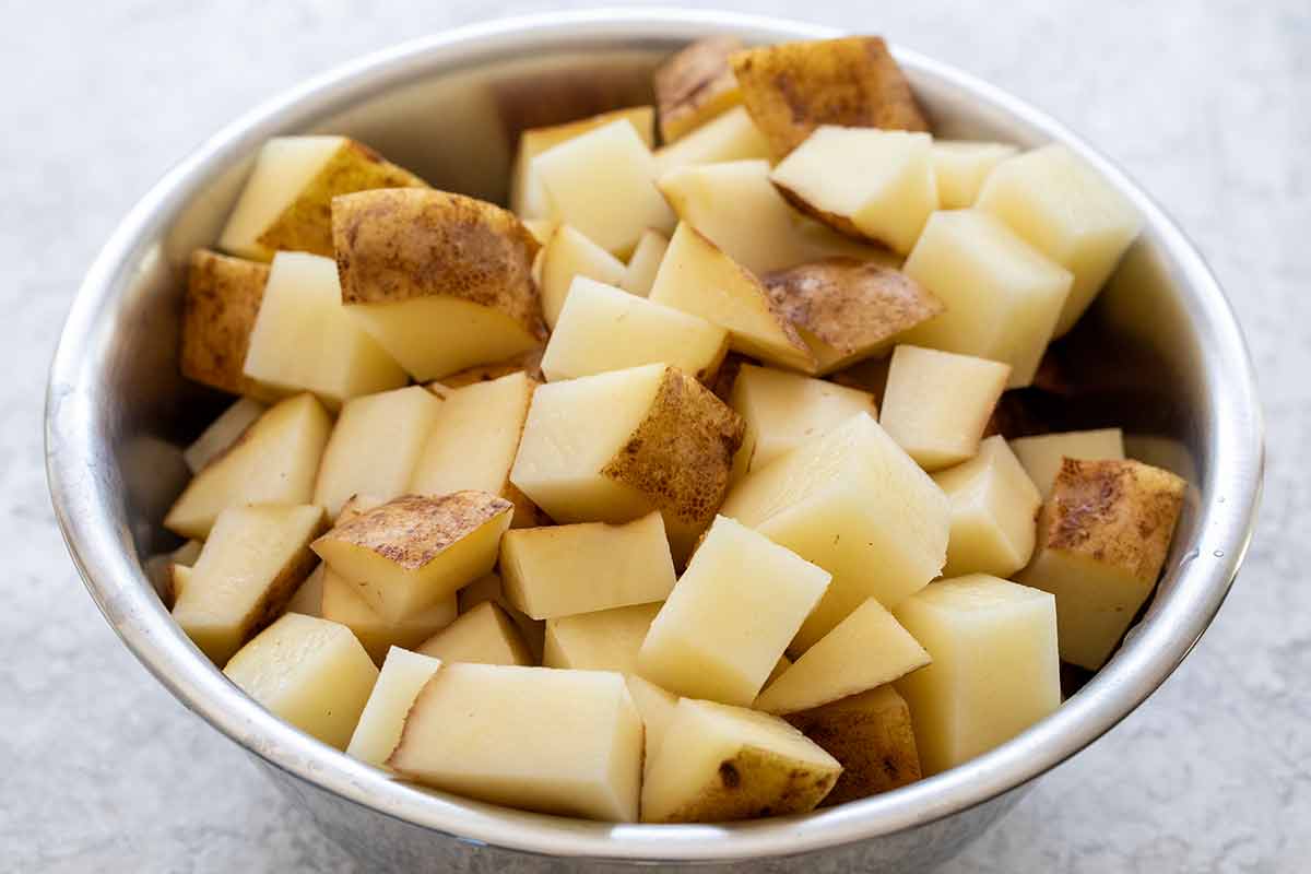 Raw Russet potatoes diced into three-quarter-inch cubes with skins on in a metal bowl.