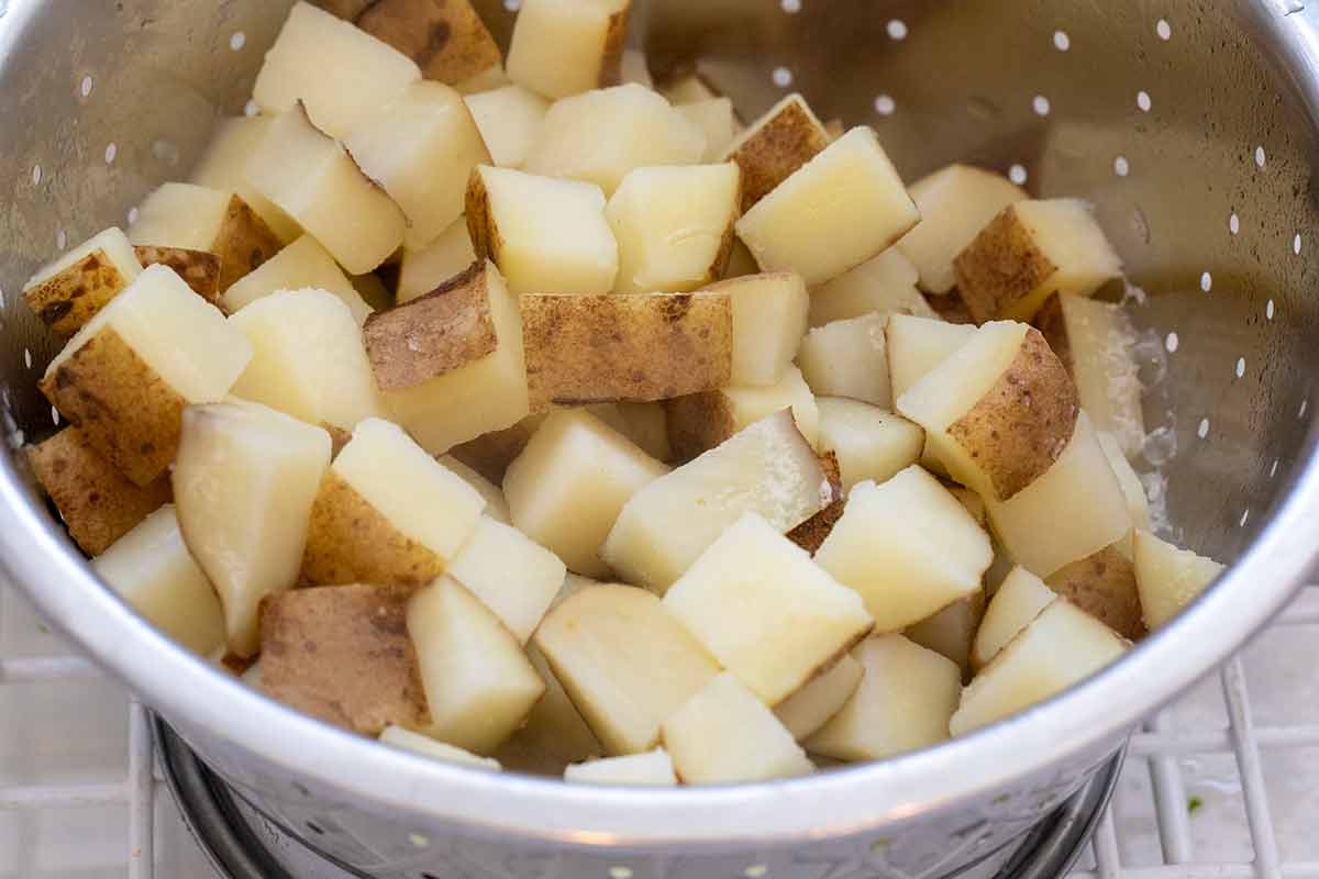 Diced parboiled potatoes draining in a stainless steel colander.