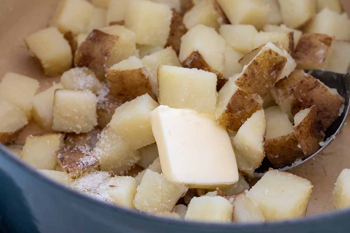 Diced parboiled potatoes in a pot topped with a pat of butter and sprinkled coarse salt.