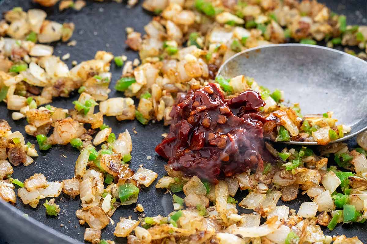Chipotle peppers being added to a pan with caramelized onions.