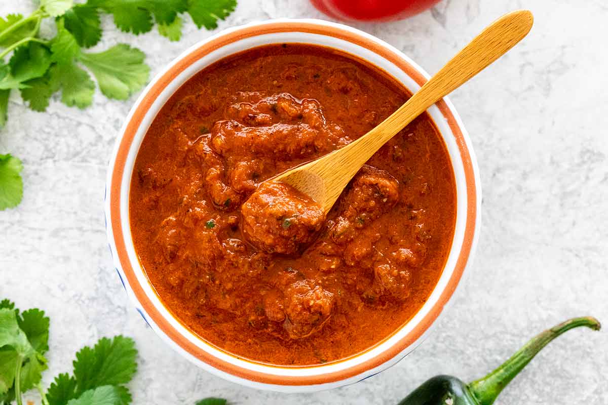 Looking down at a bowl of ranchero sauce with a wooden spoon inside.