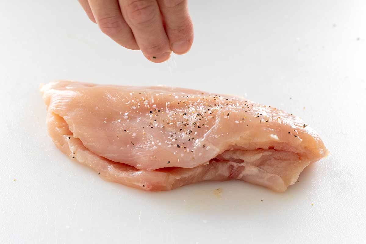 Person seasoning the chicken surface with salt and pepper.