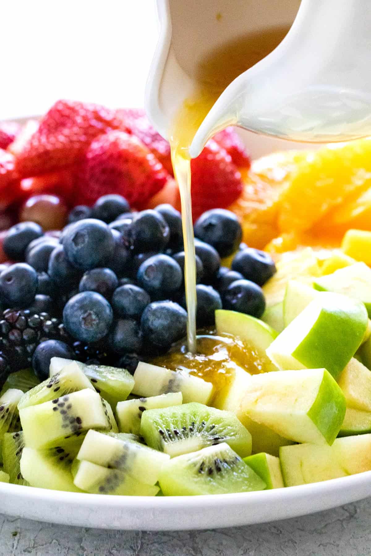 Pouring salad dressing over fruit.