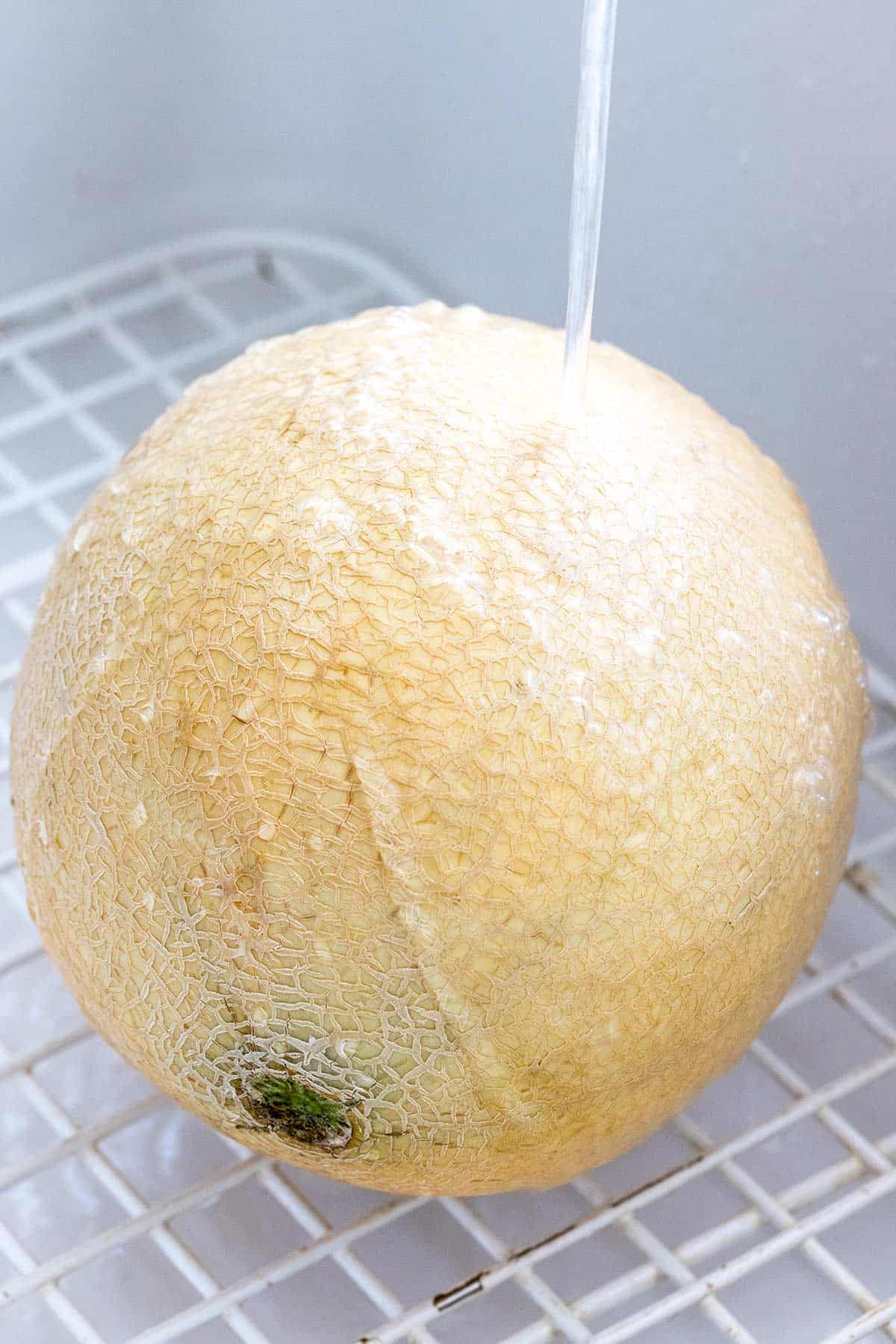 Rinsing a melon with water in a sink.