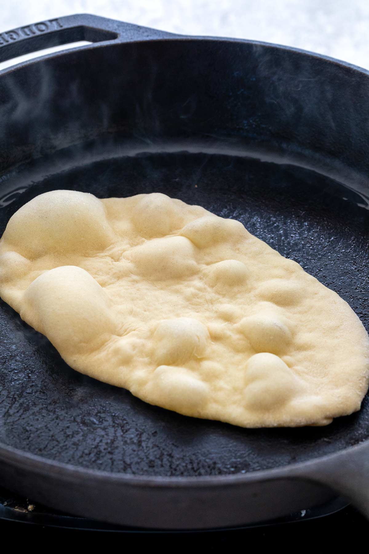 Naan bread with bubbles forming as it cooks.