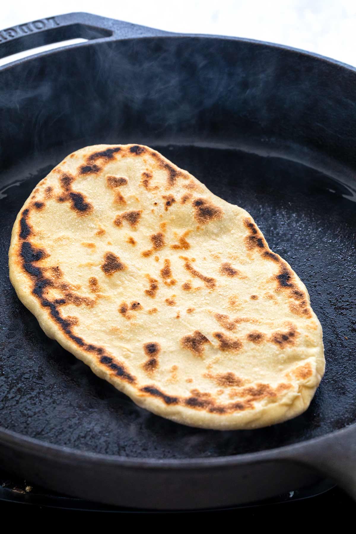 Naan bread cooking in a cast iron skillet.