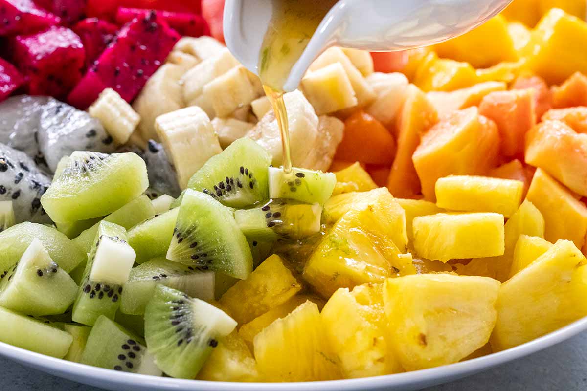 Liquid being poured over a bowl of tropical fruit.