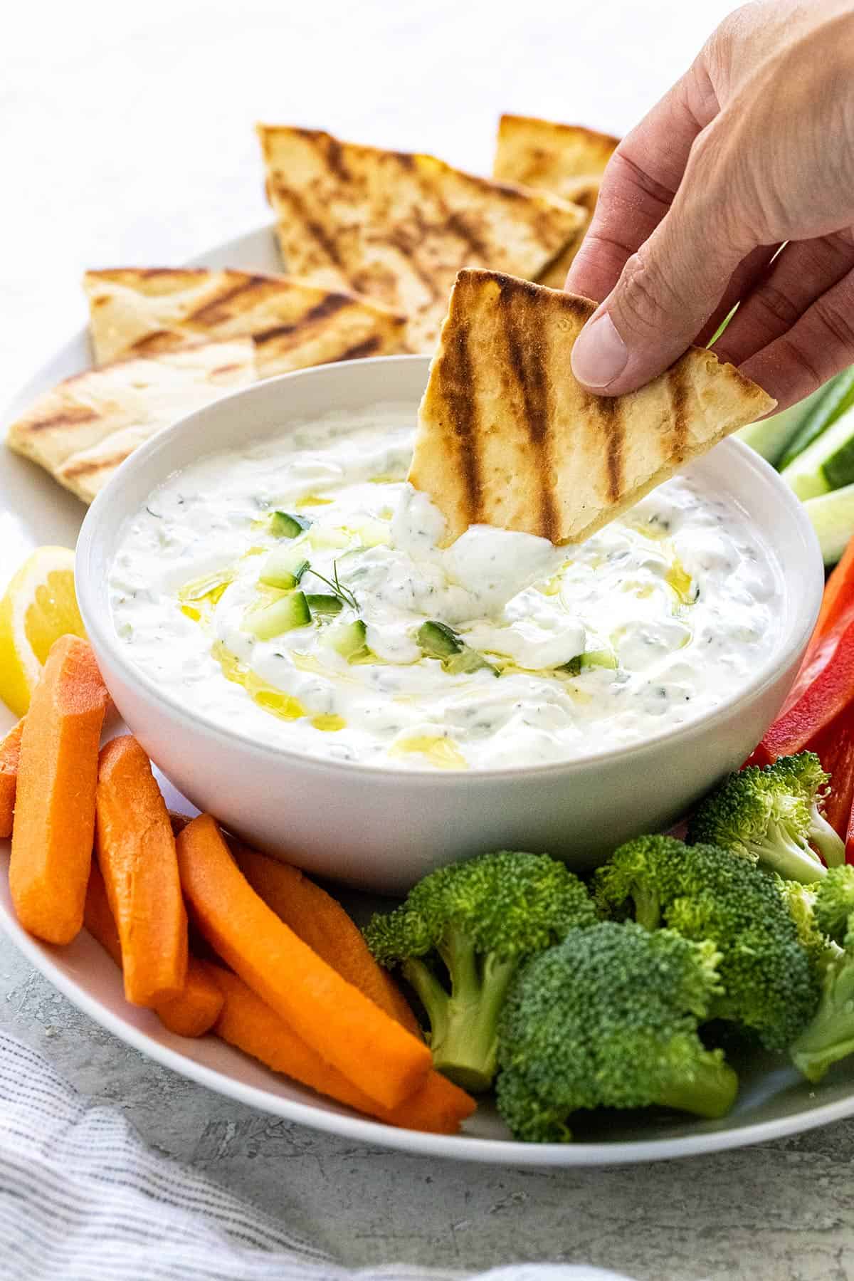 Person dipping a pita chip into a bowl of tzatziki sauce.