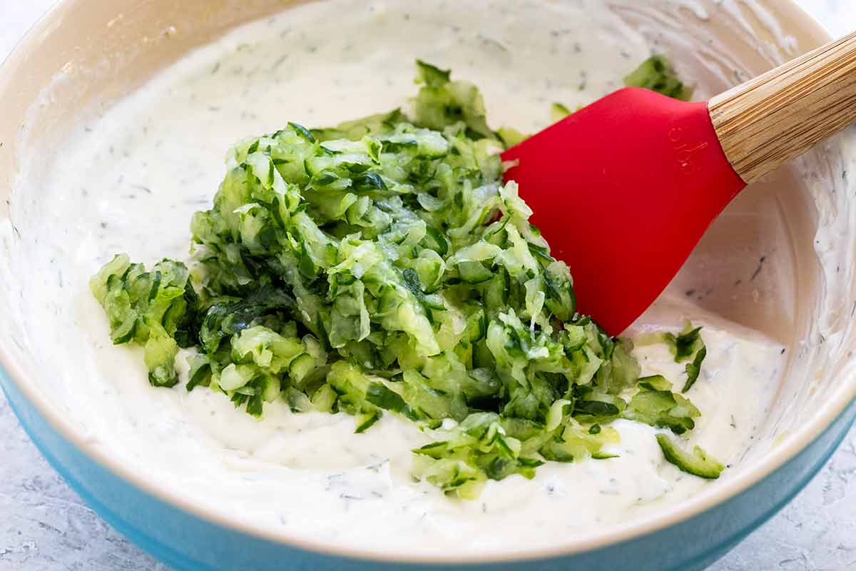 Mixing shreds of cucumber into a bowl of yogurt sauce.