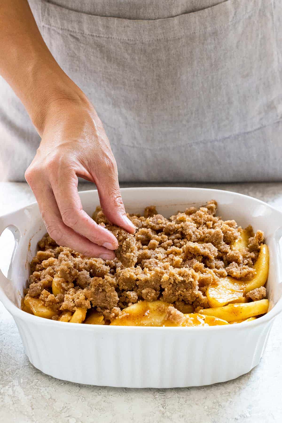 Person placing crumble topping over apple slices.