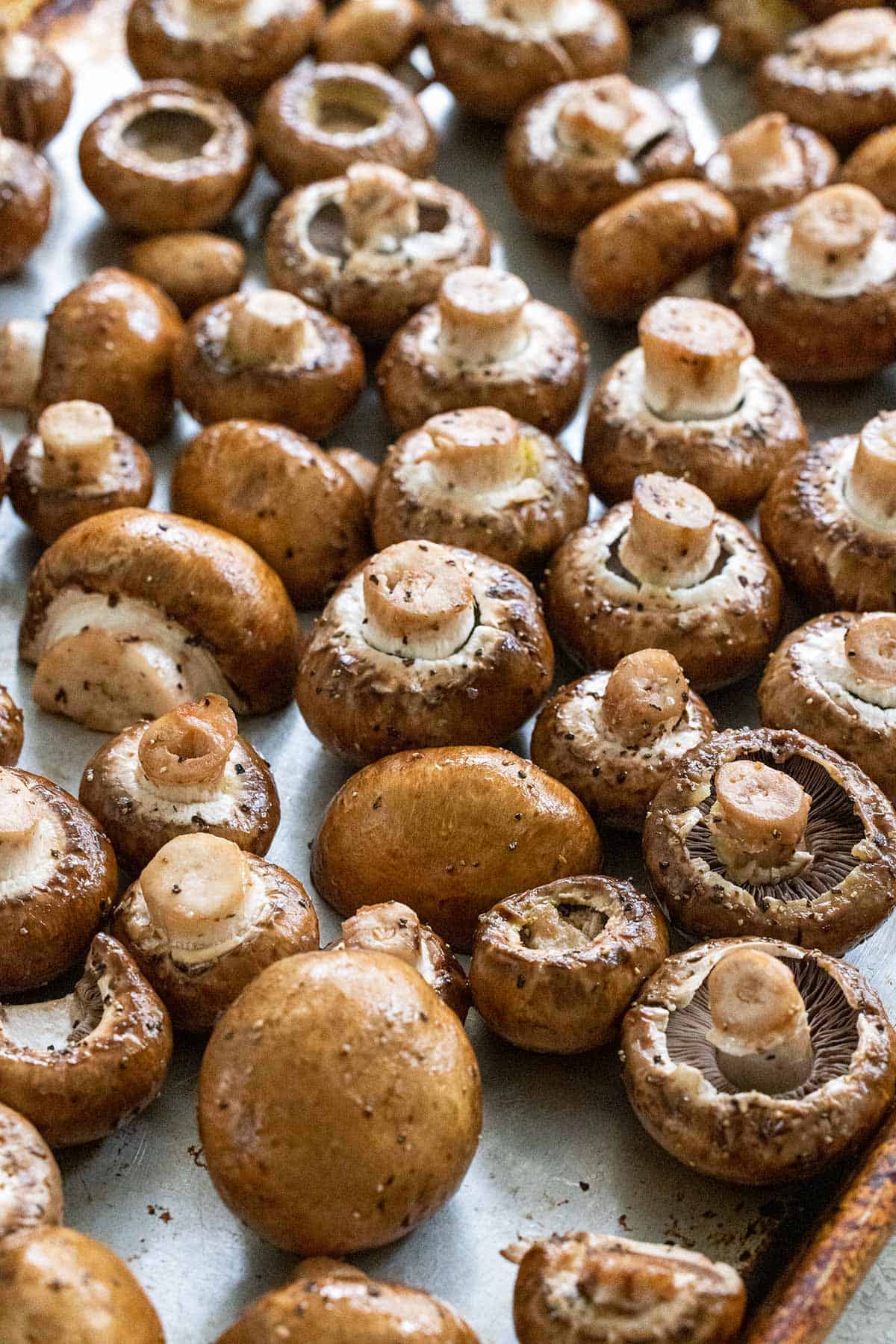 Mushrooms laid out on a sheet pan with salt and pepper sprinkled on top.