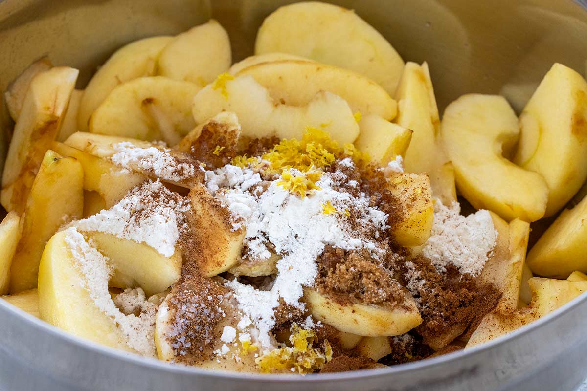 Peeled apple slices in a pot topped with flour, brown sugar, cinnamon, and lemon zest.