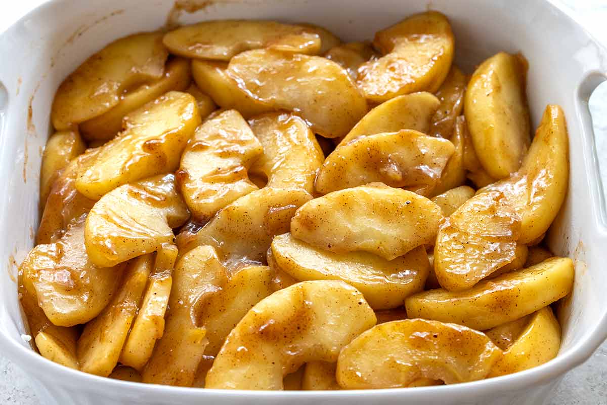 Sautéed apple slices coated in a glossy cinnamon glaze spread in a white baking dish.