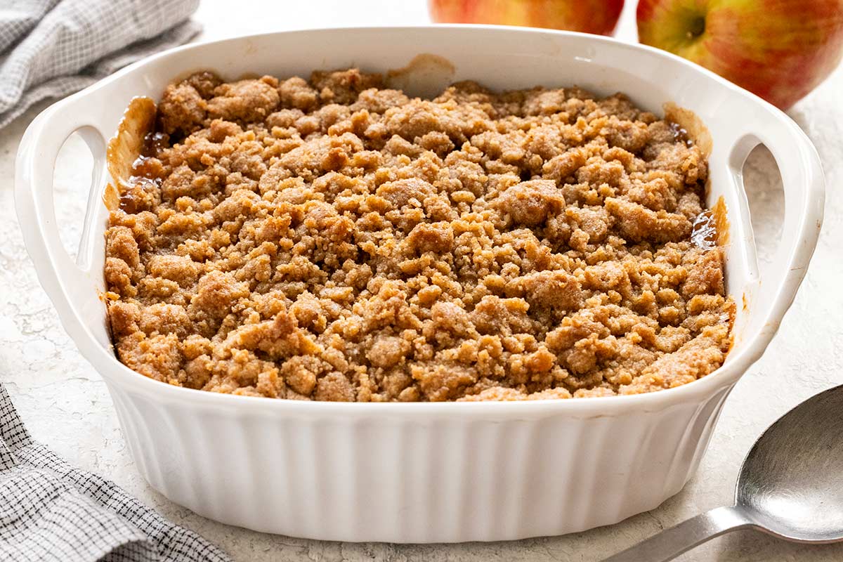 Dime-sized crumble topping spread in an even layer over pre-cooked apples in a white baking dish.